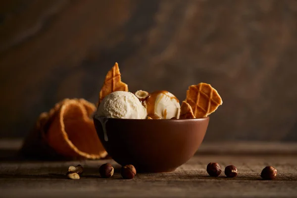 Delicious ice cream with pieces of waffle and hazelnuts in bowl on wooden surface — Stock Photo