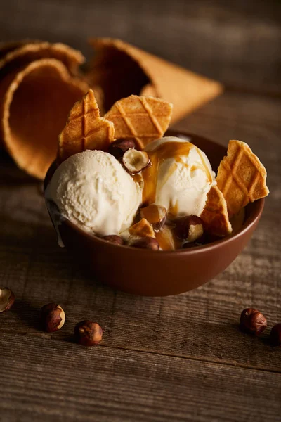 Delicioso helado con trozos de waffle y avellanas en tazón sobre mesa de madera - foto de stock