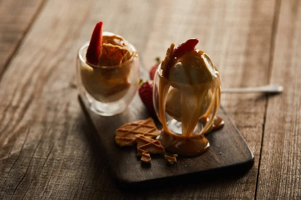 Delizioso gelato in bicchieri con fragole e caramello sul tagliere di legno — Foto stock