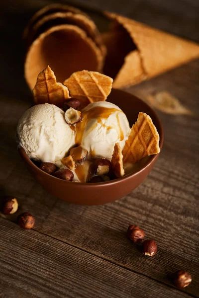 Delicious ice cream with pieces of waffle and hazelnuts in bowl on wooden table — Stock Photo