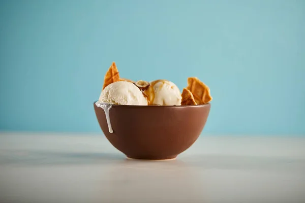 Selective focus of bowl with delicious melting ice cream scoops and pieces of waffle on blue — Stock Photo