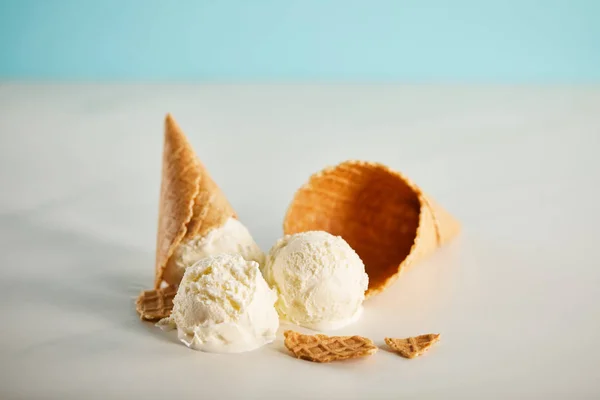 Boules de crème glacée fondantes et cône de gaufre sur bleu et gris — Photo de stock