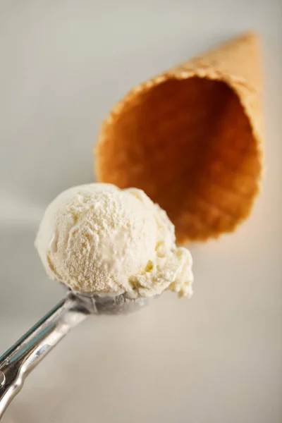 Selective focus of ice cream scoop in spoon and waffle cone on grey — Stock Photo