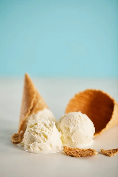 Boules de crème glacée fondantes et cône de gaufre sur bleu et gris avec espace de copie — Photo de stock