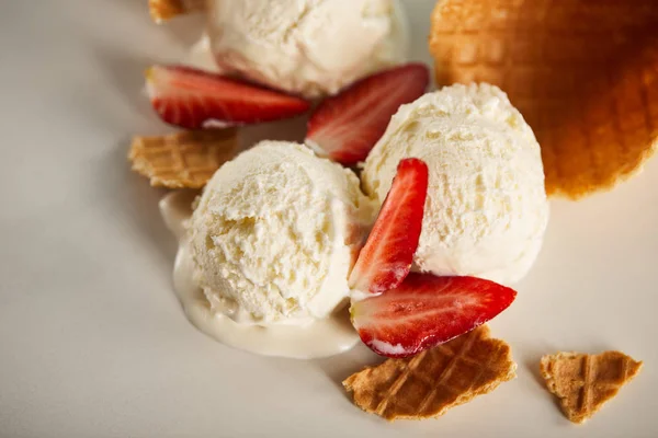 Vista de cerca de piezas de gofre y delicioso helado derretido con fresas en gris - foto de stock