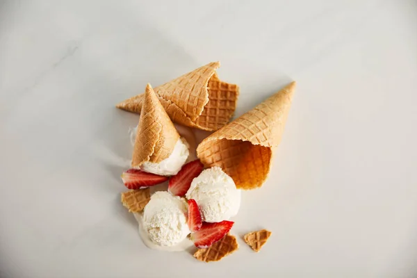Вид сверху на шишки и вкусное тающее мороженое с клубникой на серой поверхности — стоковое фото
