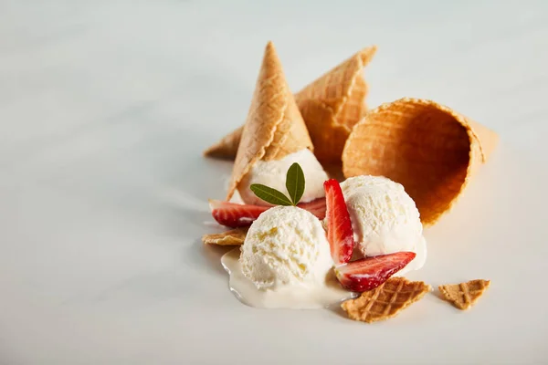 Cones de waffle e delicioso sorvete derretendo com morangos na mesa cinza com espaço de cópia — Fotografia de Stock
