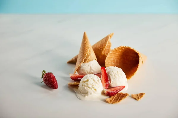 Cones de waffle e delicioso sorvete derretendo com morangos na mesa cinza — Fotografia de Stock