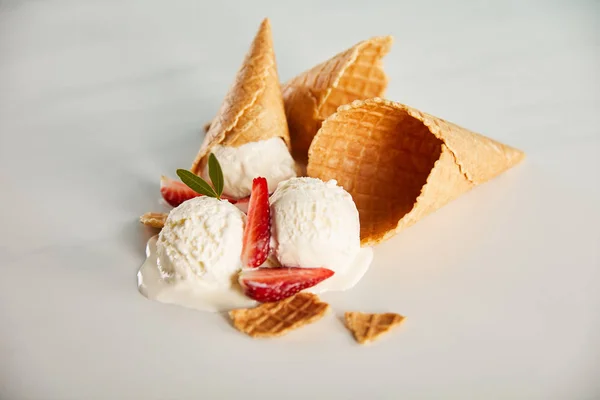 Conos de gofre y delicioso helado de fusión con fresas en la mesa gris - foto de stock