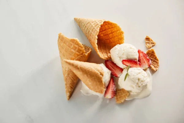 Vista superior de conos y deliciosos helados derretidos con fresas en gris - foto de stock