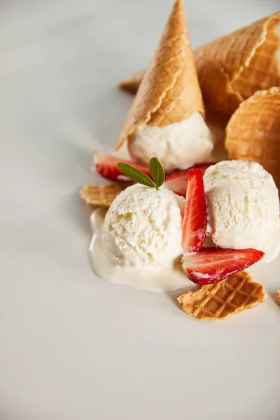 Cones de waffle e delicioso sorvete derretendo com morangos em cinza — Fotografia de Stock