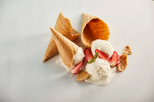 Waffelzapfen und schmelzendes Eis mit Erdbeeren auf grau — Stockfoto