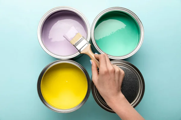 Vue partielle de la femme avec brosse et boîtes de peinture sur la surface bleue — Photo de stock