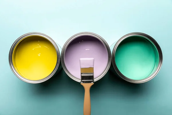 Vista superior de três latas com tintas e pincel na superfície azul — Fotografia de Stock