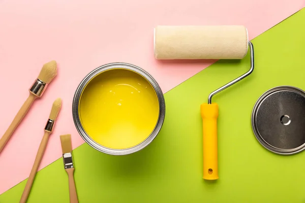 Top view of tin with yellow paint, brushes and paint roller on pink and green surface — Stock Photo