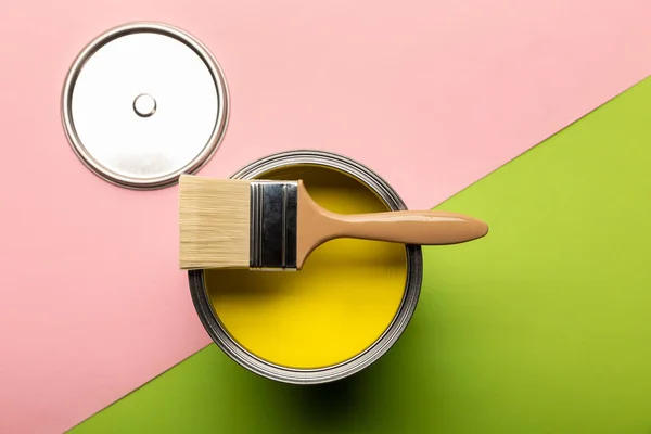 Top view of tin with yellow paint and brush on pink and green surface — Stock Photo