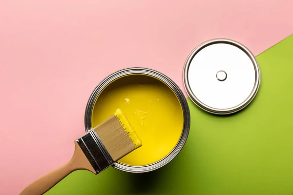 Верхний вид олова с желтой краской и кистью на розовую и зеленую поверхность — стоковое фото