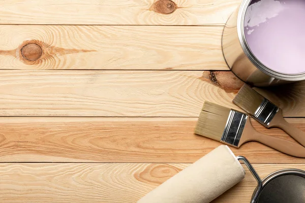 Vista superior de escovas, estanho de tinta roxa e rolo de pintura na superfície de madeira — Fotografia de Stock