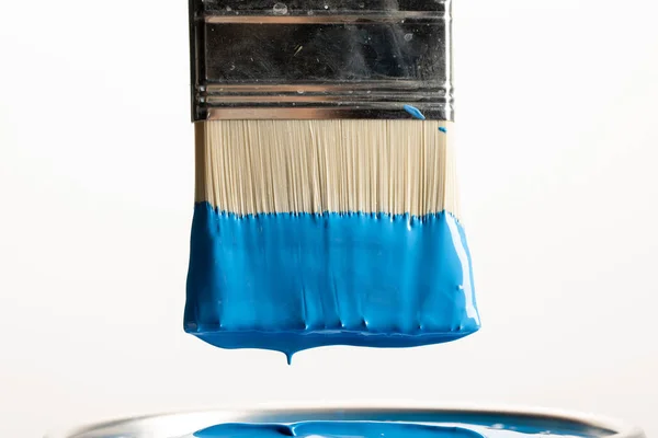 Крупный план кисти с синей краской поверх банки, изолированной на белом — стоковое фото