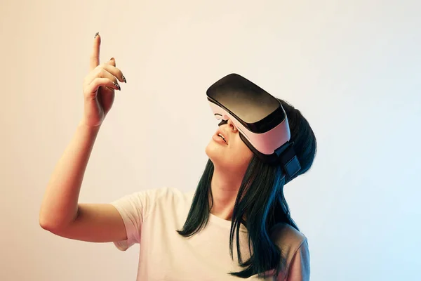 Brunette woman wearing virtual reality headset and pointing with finger on beige and blue — Stock Photo