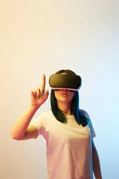 Enfoque selectivo de la mujer señalando con el dedo mientras usa auriculares de realidad virtual en beige y azul - foto de stock