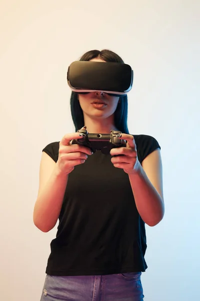 KYIV, UKRAINE - APRIL 5, 2019: Brunette woman playing video game while wearing virtual reality headset on beige and blue — Stock Photo