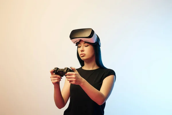 KYIV, UKRAINE - APRIL 5, 2019: Young woman looking at joystick while wearing virtual reality headset on beige and blue — Stock Photo