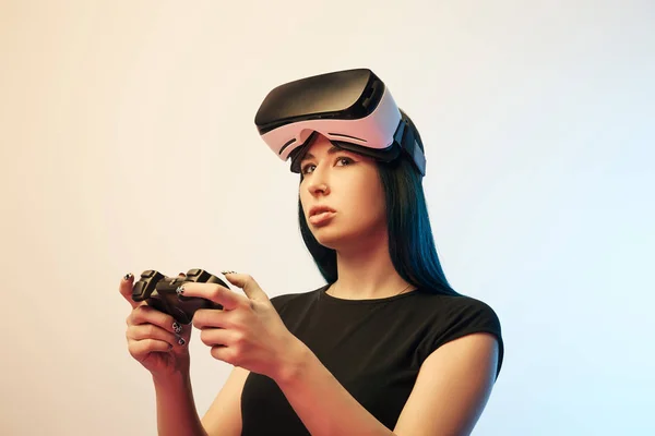 KYIV, UCRANIA - 5 DE ABRIL DE 2019: Hermosa mujer morena jugando a videojuegos con auriculares de realidad virtual en beige y azul - foto de stock