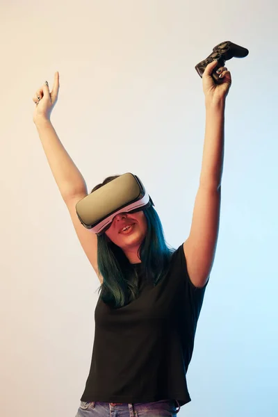 KYIV, UCRANIA - 5 DE ABRIL DE 2019: Mujer morena alegre sosteniendo el joystick mientras hace gestos con auriculares de realidad virtual en beige y azul - foto de stock