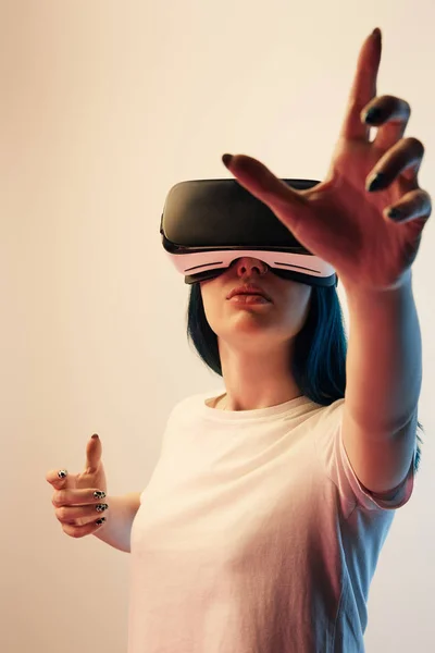 Messa a fuoco selettiva di bruna ragazza indossa auricolare realtà virtuale e gesticolare sul beige — Foto stock