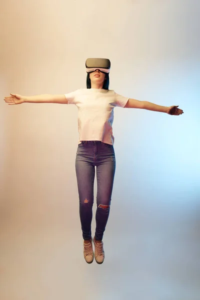 Mujer joven en auriculares de realidad virtual con las manos extendidas levitando sobre beige y azul - foto de stock