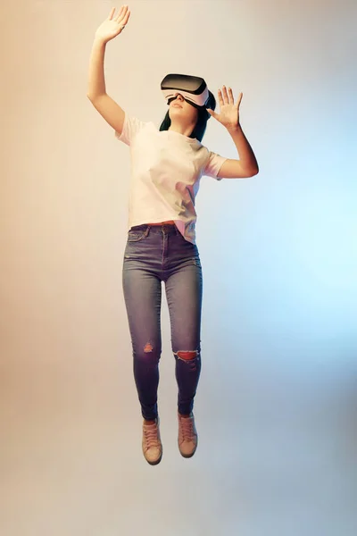 Молодая женщина в наушниках виртуальной реальности жестикулирует, левитируя на бежевом и синем — стоковое фото