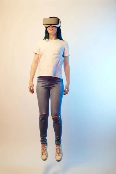 Молодая женщина в наушниках виртуальной реальности, левитирующая на бежевом и синем — стоковое фото
