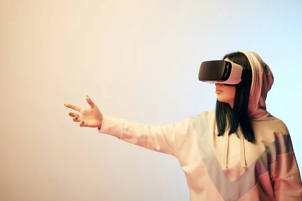 Young brunette girl wearing virtual reality headset and gesturing on beige and blue — Stock Photo