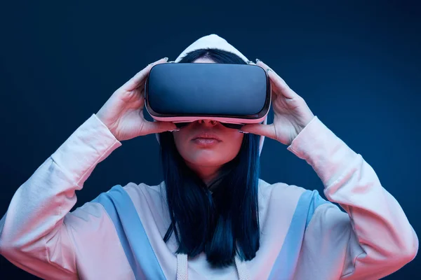 Brunetta ragazza in cappuccio toccare realtà virtuale auricolare su blu — Foto stock