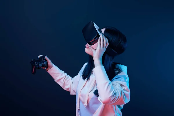 KYIV, UKRAINE - APRIL 5, 2019: Brunette woman holding joystick while touching virtual reality headset on blue — Stock Photo