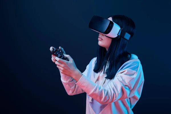 KYIV, UCRANIA - 5 DE ABRIL DE 2019: Mujer morena sosteniendo el joystick mientras juega videojuegos con auriculares de realidad virtual en azul - foto de stock
