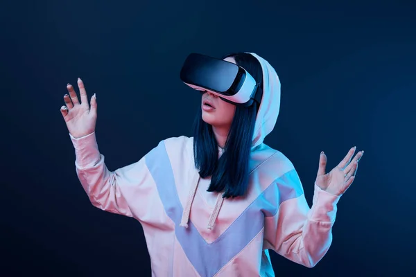 Surprised brunette woman gesturing while using virtual reality headset on blue — Stock Photo