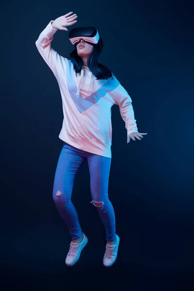 Young woman gesturing while using virtual reality headset and jumping on blue — Stock Photo