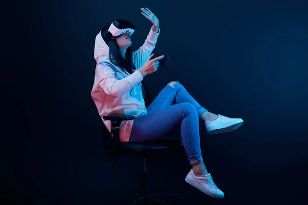 KYIV, UKRAINE - APRIL 5, 2019: Brunette woman holding joystick and gesturing while wearing virtual reality headset on blue — Stock Photo