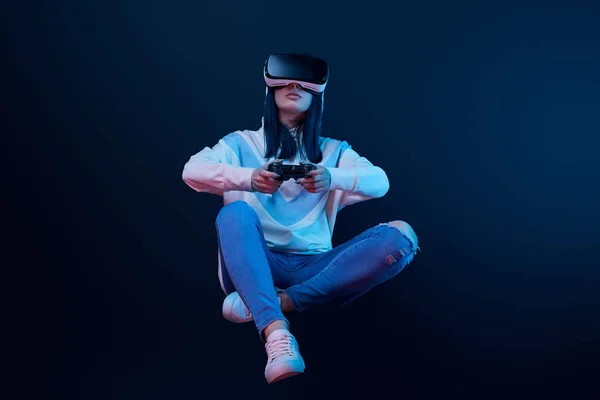 KYIV, UKRAINE - 5 de abril de 2019: Mulher segurando o joystick enquanto levita, jogando videogame e vestindo fones de ouvido de realidade virtual em azul — Fotografia de Stock