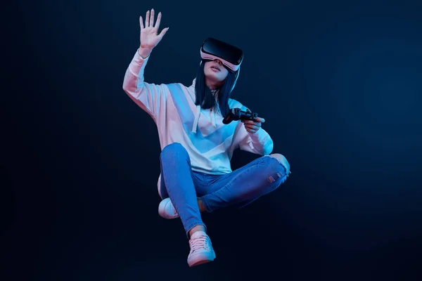 KYIV, UKRAINE - 5 de abril de 2019: Mulher segurando joystick e levitando enquanto gesticula e vestindo fone de ouvido de realidade virtual em azul — Fotografia de Stock