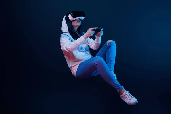 KYIV, UKRAINE - APRIL 5, 2019: Young woman in virtual reality headset levitating and holding joystick on blue — Stock Photo