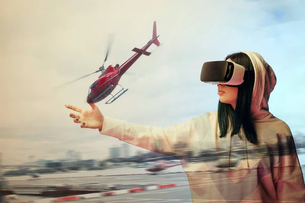 Double exposure of brunette girl gesturing while using virtual reality headset and helicopter flying near buildings — Stock Photo