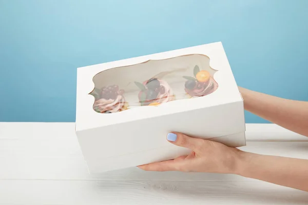 Vue partielle de femme tenant boîte avec cupcakes isolé sur bleu — Photo de stock