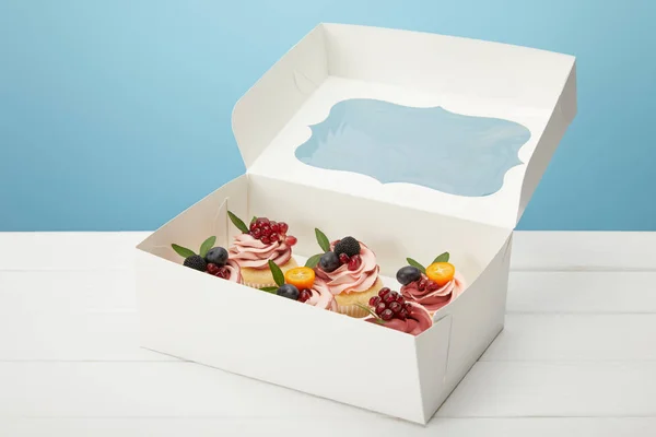 Caixa com cupcakes na superfície branca isolada em azul — Fotografia de Stock