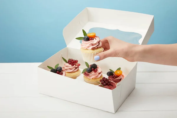 Vista cortada de mulher segurando cupcake doce isolado em azul — Fotografia de Stock