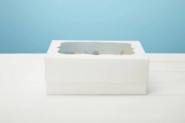 Scatola con cupcake su superficie bianca isolata su blu — Foto stock