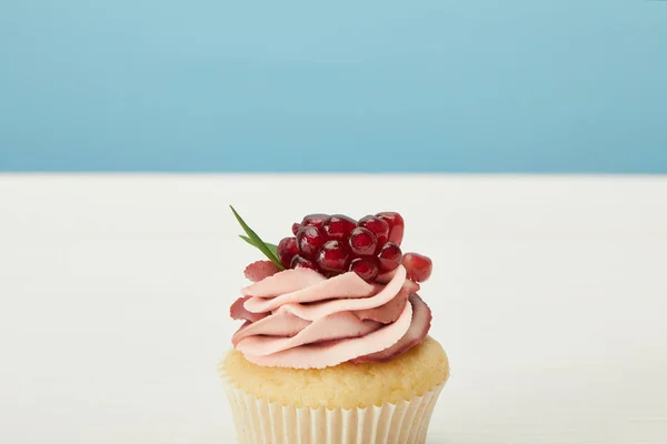 Cupcake saboroso com granada e creme na superfície branca isolada em azul — Fotografia de Stock