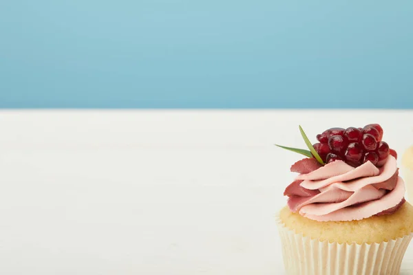 Sabroso cupcake con granate y crema en la superficie blanca aislado en azul - foto de stock